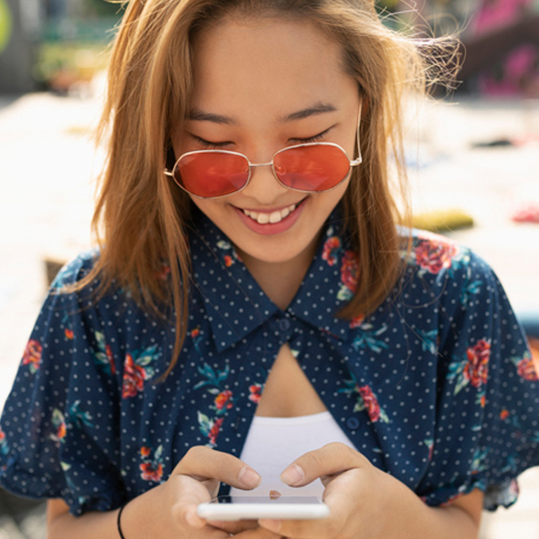 a woman wearing rose colored sunglasses, texting on smartphone