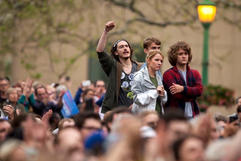 students standing in a crowd, one has his fist raised