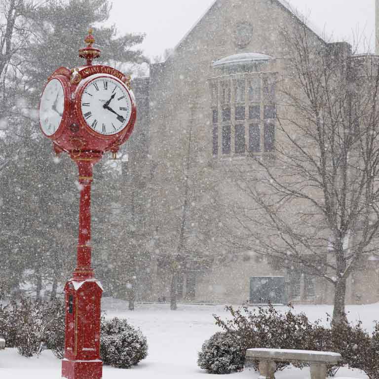 a tall red clock on the IU campus on a snowy day 